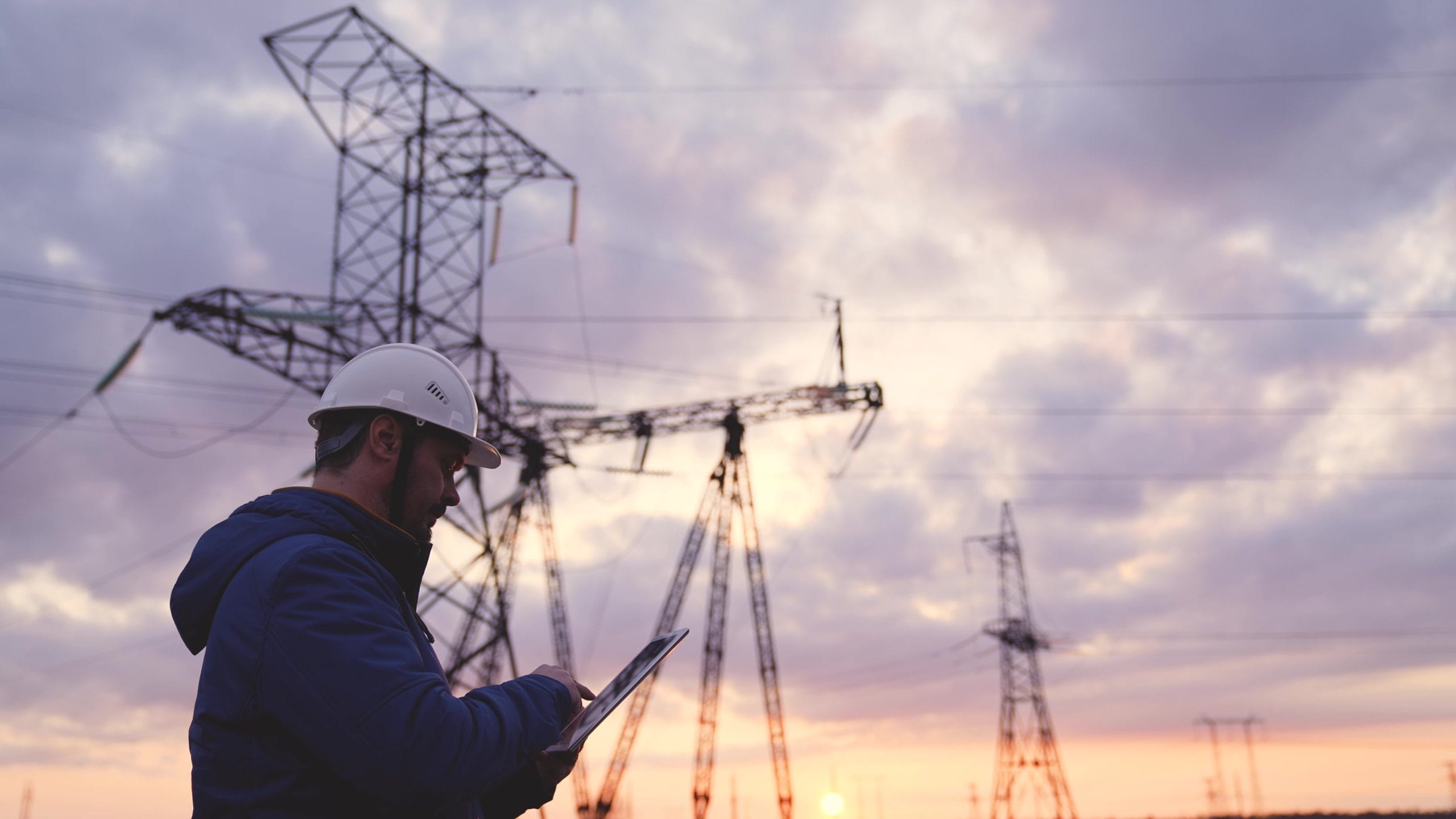 An engineer at a high voltage power plant works in a tablet at sunset in the sky, electrical energy design, industry concept, modern business technologies, an electrician reads a project on a gadget display.